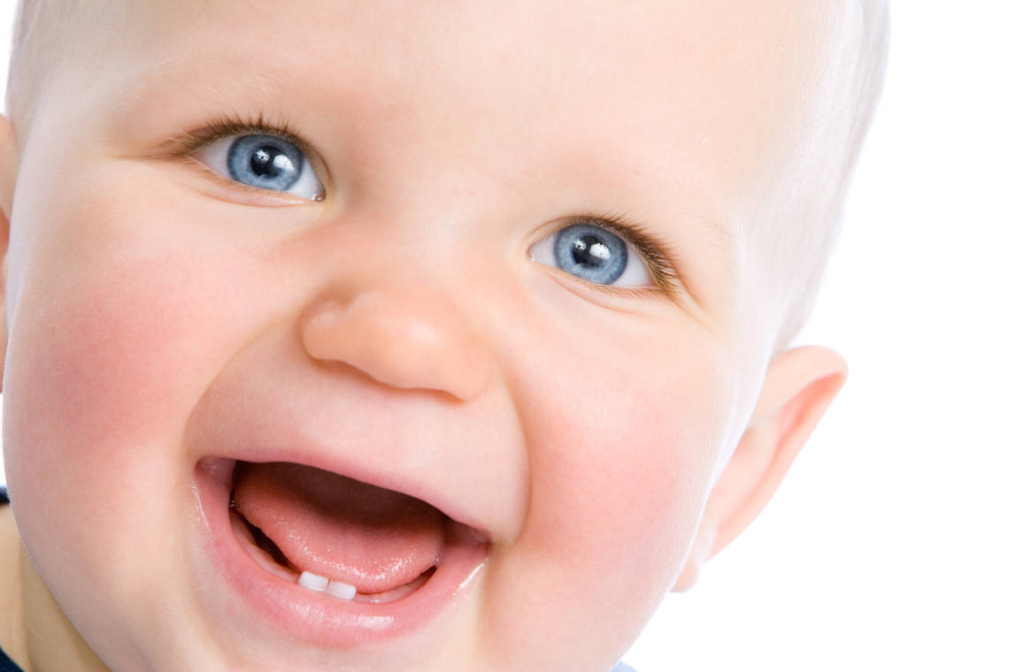 Lachendes Baby mit blauen Augen. Zwei kleine Zähne in der unteren Zahreihe scheinen hervor.